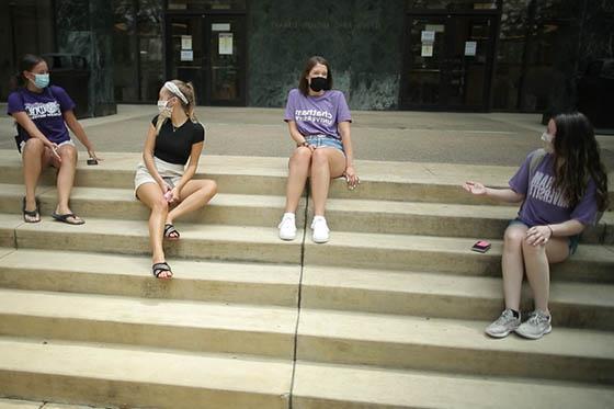 四名波胆网站女学生的照片, wearing masks and Chatham t-shirts, all sit socially distant on the library steps